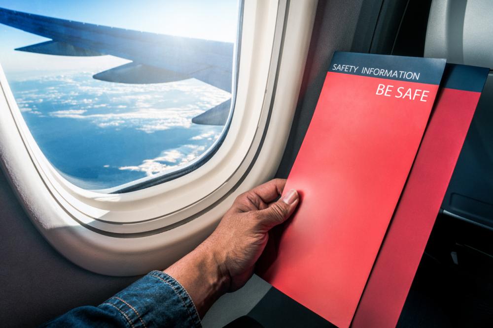 person holding safety informtion pamphlet on airplane