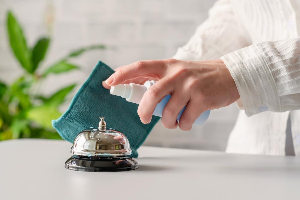 woman's hand sanitizes reception desk bell