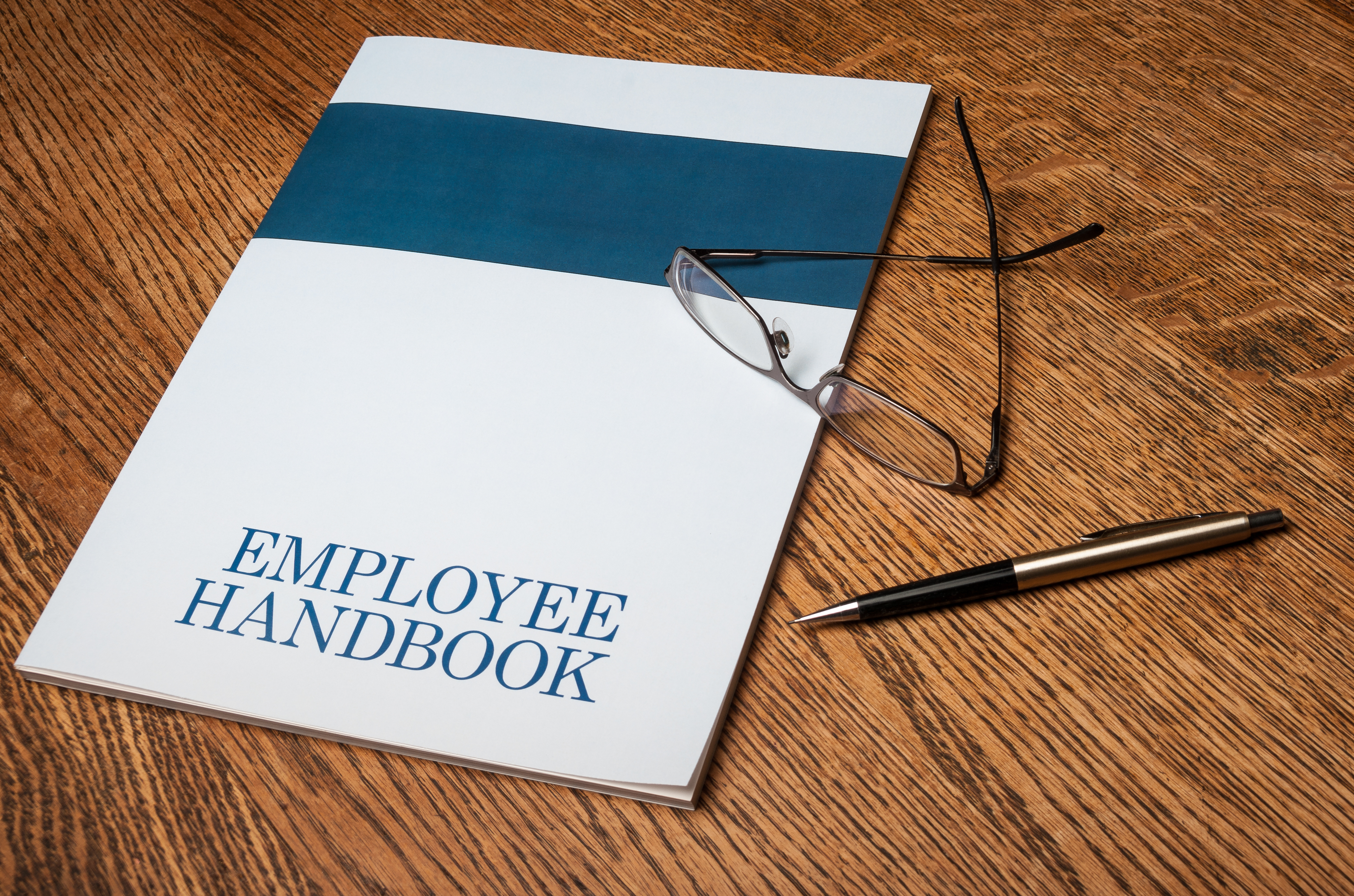 employee handbook, pen, glasses on a wooden surface