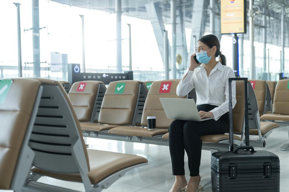 Social distancing, businesswoman wearing face mask sit working with laptop in airport