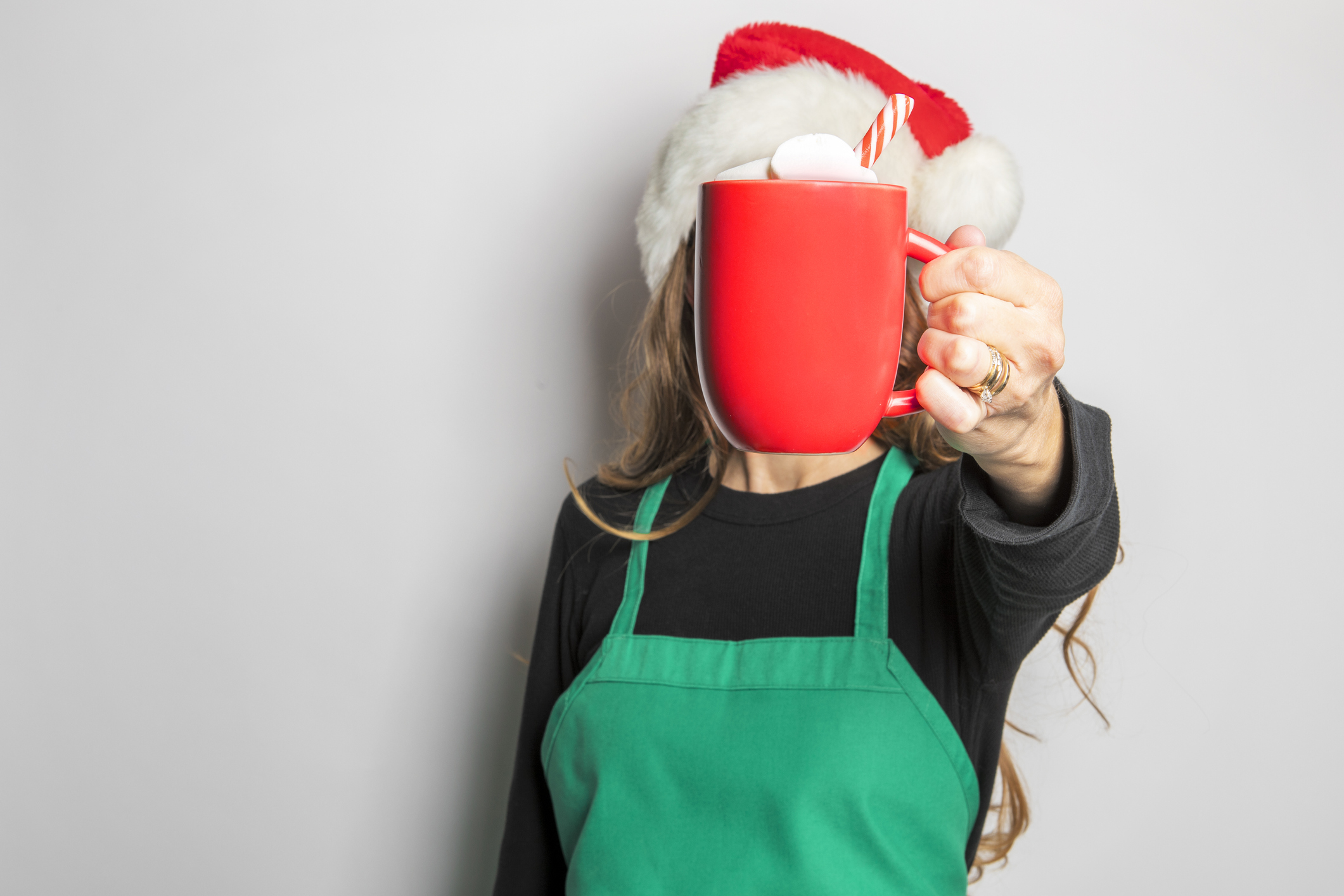 barista wearing a santa hat and holding a red cup of hot cocoa in front of her face
