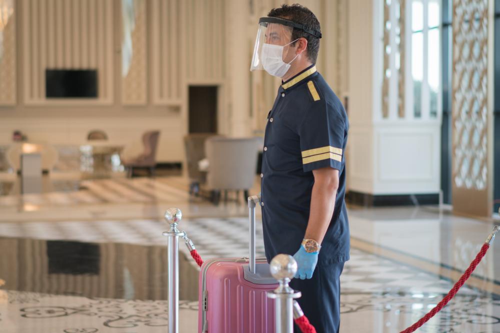 Bellboy wearing a 2 face masks and gloves while handling luggage