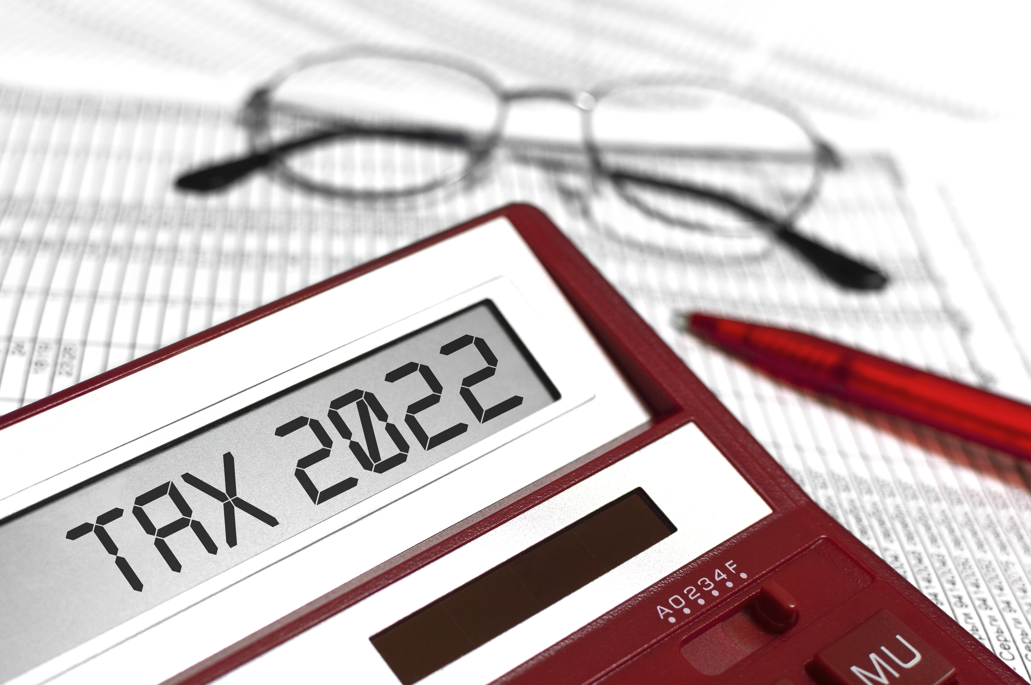 red calculator spelling out Tax 2022 next to a red pen and glasses