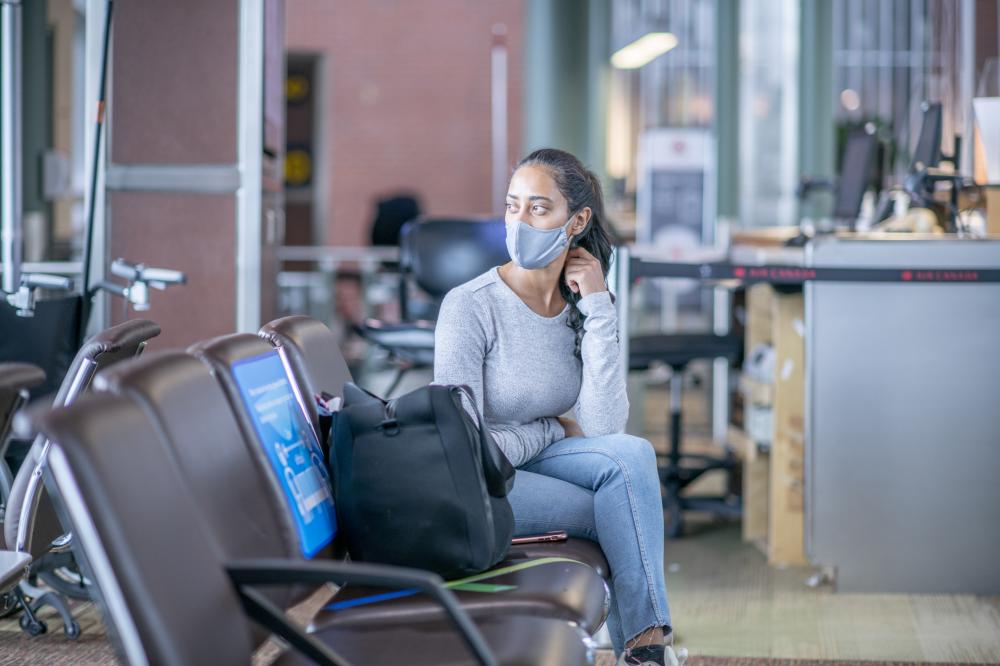 A young woman of Middle Eastern ethnicity is sitting at the airport departure gate. She is
wearing a face mask to prevent the spread of germs during the coronavirus pandemic.