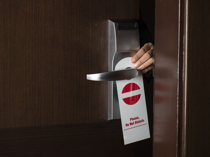 person placing Do Not Disturb sign on hotel room door