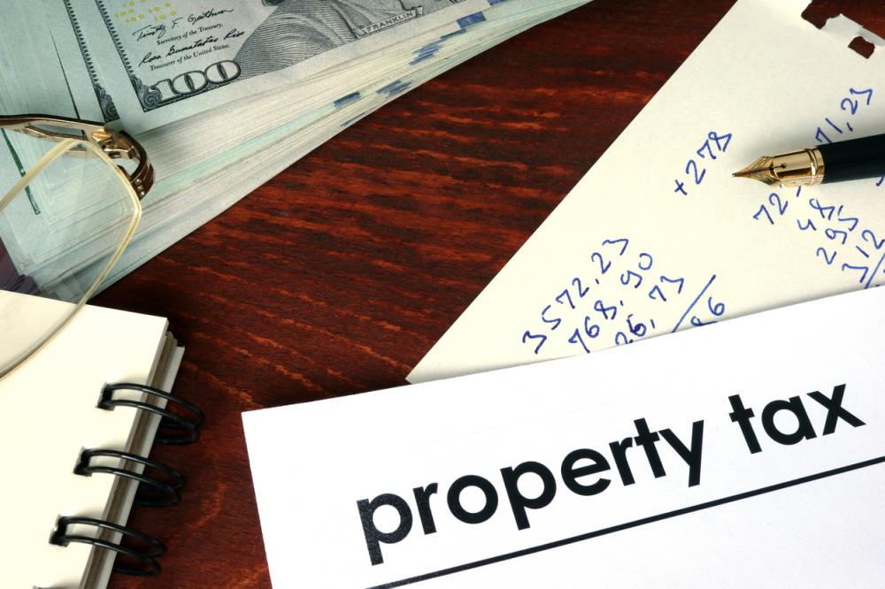 Property tax written on a paper; stack of bills; pen; glasses; journal