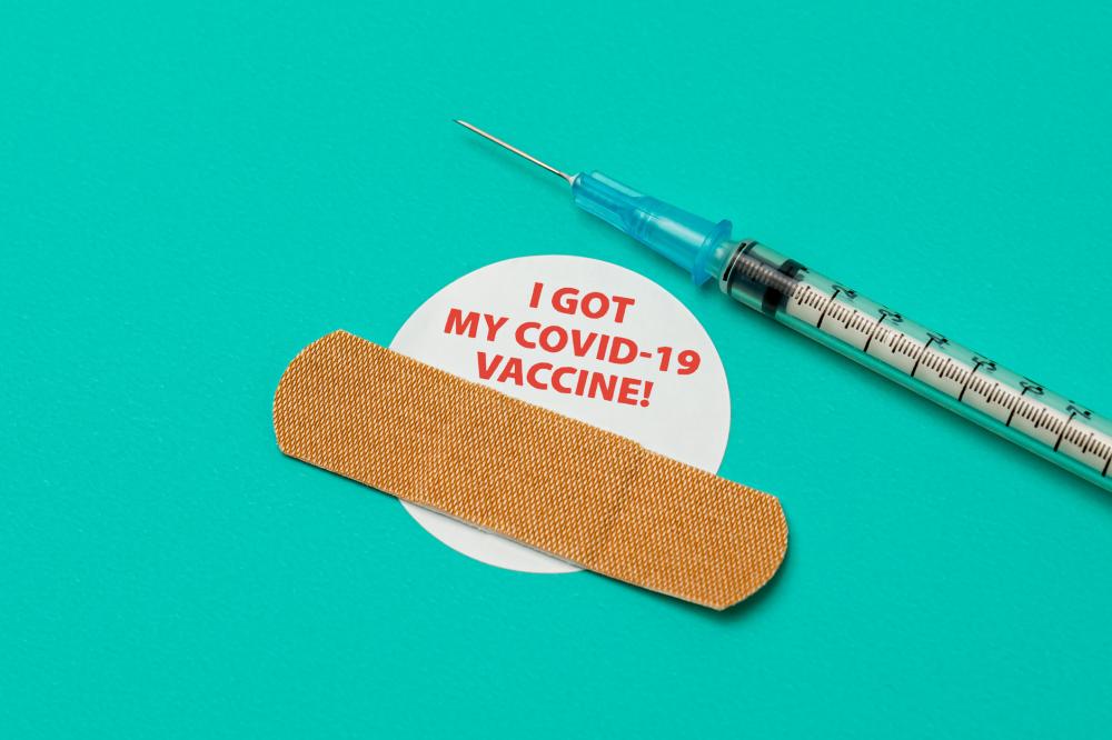 Needle, band-aid, and a sticker that reads "I got my covid-19 vaccine!" against a teal background