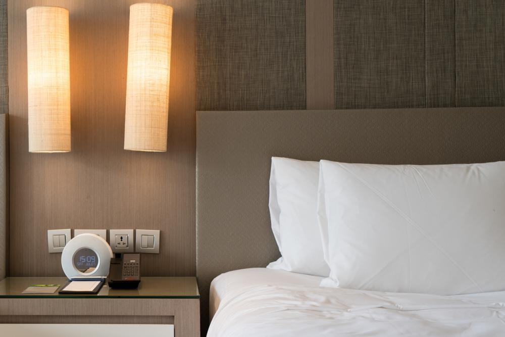 closeup of bed, bedside table with alarm clock and phone, in a hotel