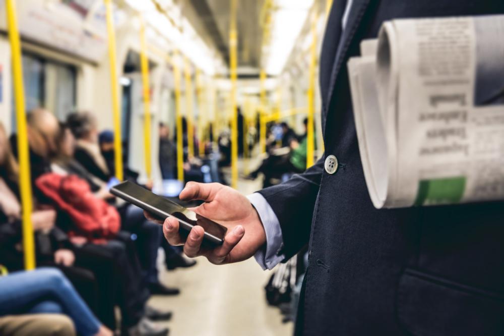 businessman holds a cell phone and newspaper while riding a train