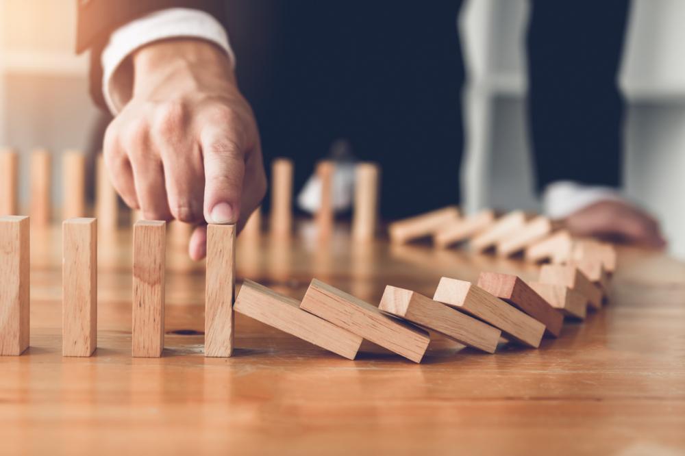 businesman stopping wooden block from falling in the line of domino risk
