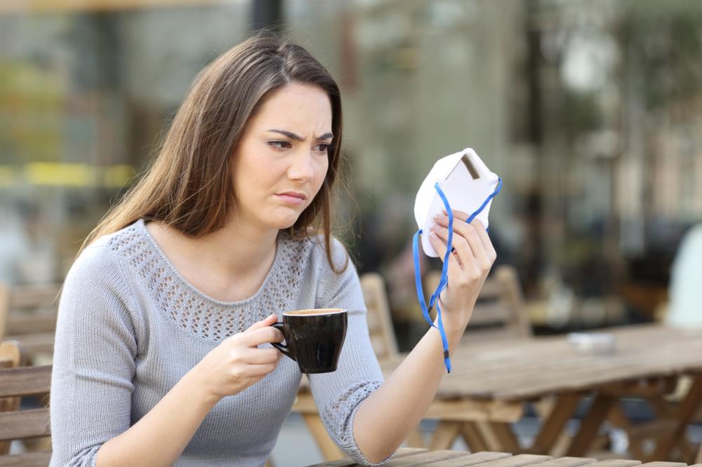 doubtful woman looking at protective mask in a coffee shop