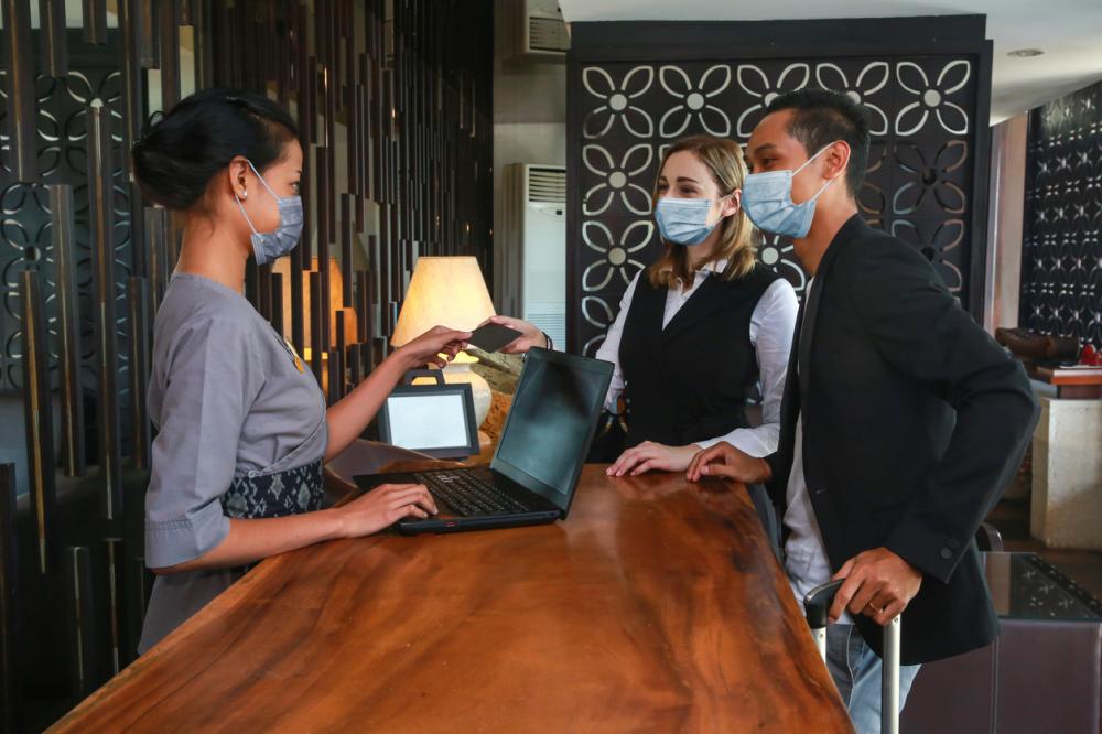 guests wearing face masks check into hotel with employee wearing a face mask