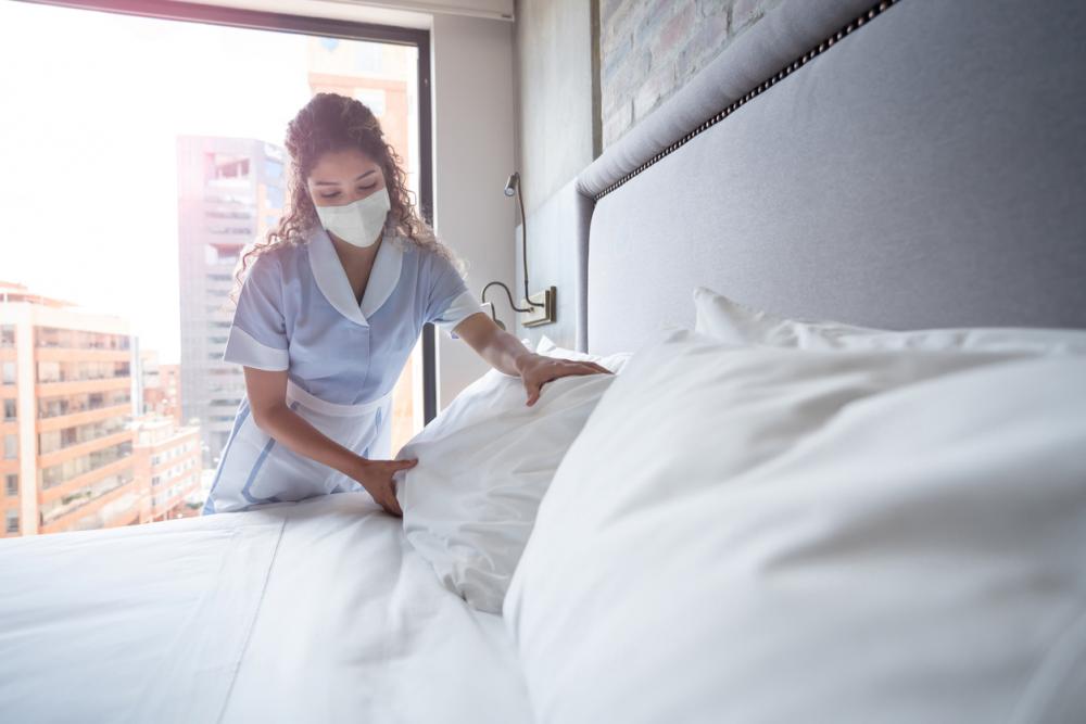 Hotel maid making a bed while wearing a mask
